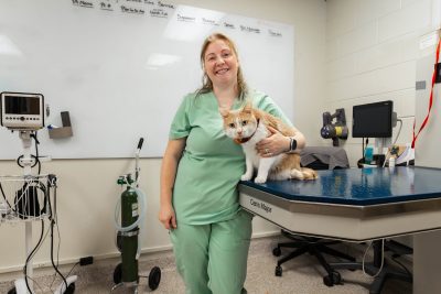 LVT in green scrubs standing with an orange cat.